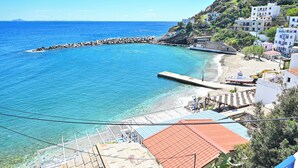 A coastal town with clear blue waters, a rocky breakwater, and buildings with red-tiled roofs.