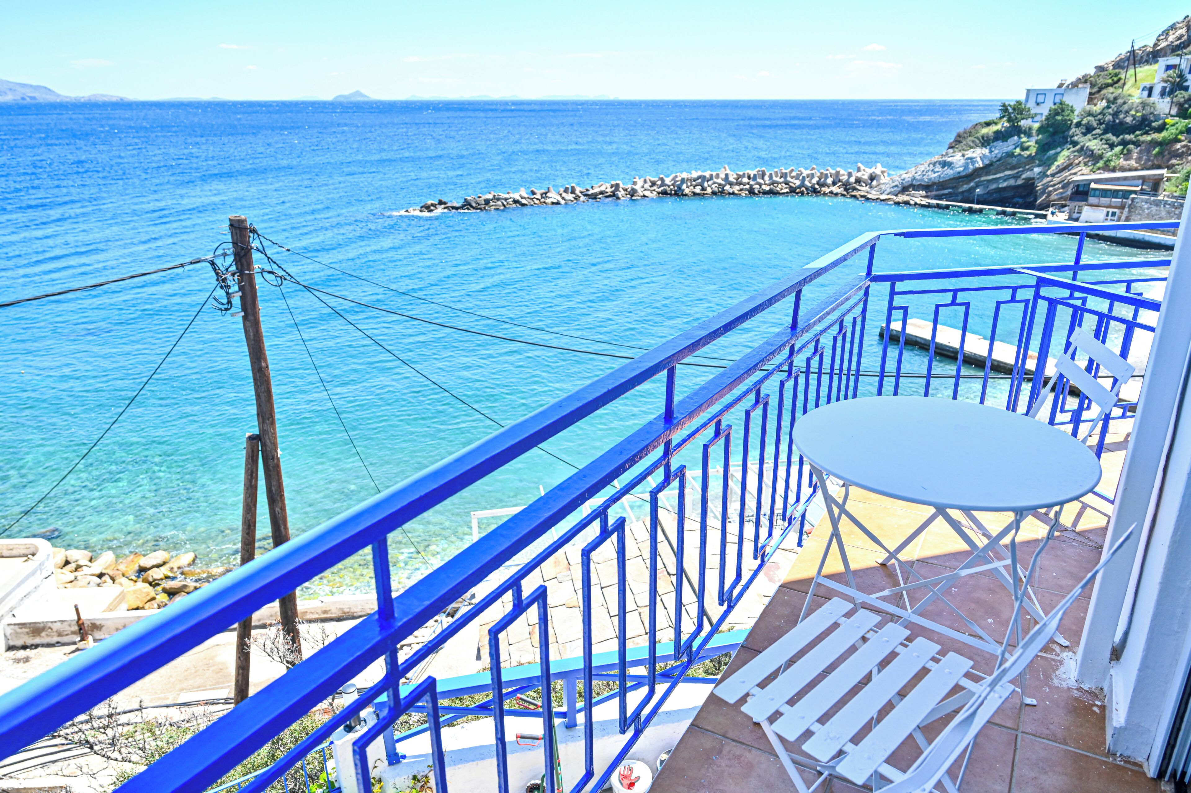 A balcony with a view of the sea, a white table, and blue railings.