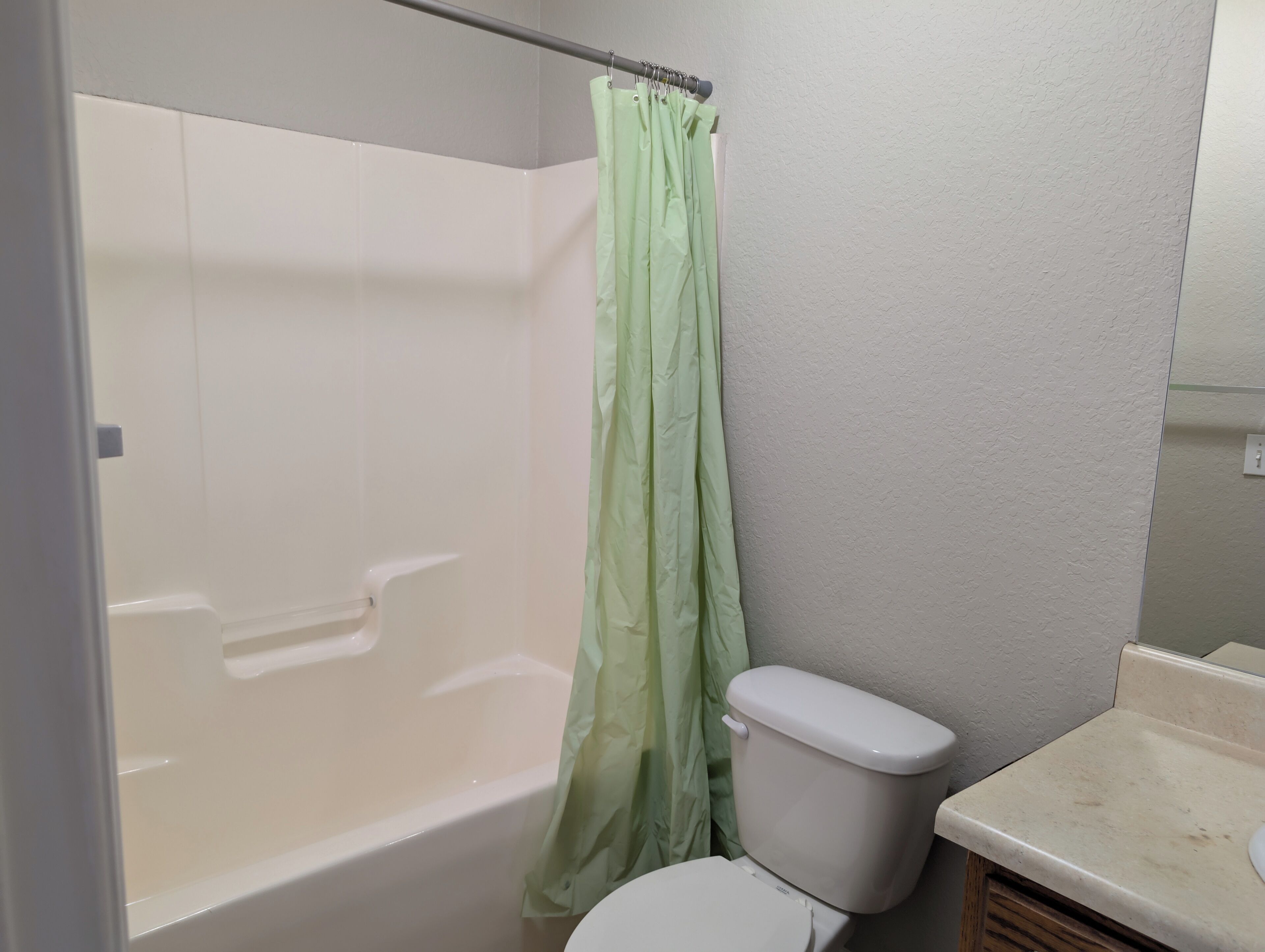 A bathroom with a bathtub, toilet, and a green shower curtain.