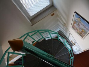 Eine Wendeltreppe mit türkisblauen Geländern und einem mit Teppich belegten schwarzen Boden, die zu einer Plattform mit einem Fenster und einer an der Wand hängenden Karte führt.