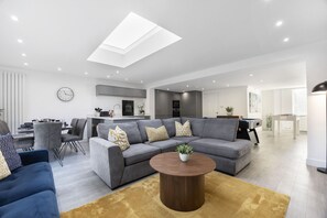 A modern living room with a sectional sofa, a coffee table, and a dining area with a table and chairs. - Fantastic 3 Bedroom Home in Gloucester City (Gloucetser)