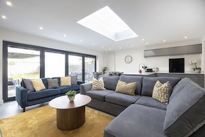 A modern living room with a grey sectional sofa, a round coffee table, and a large window providing a view of the outdoors. - Fantastic 3 Bedroom Home in Gloucester City (Gloucetser)