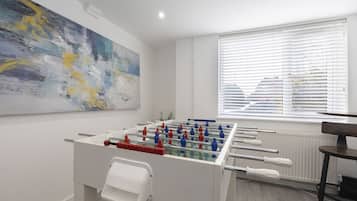 Een moderne kamer met een tafelvoetbaltafel, een groot abstract schilderij en een raam met luxaflex.