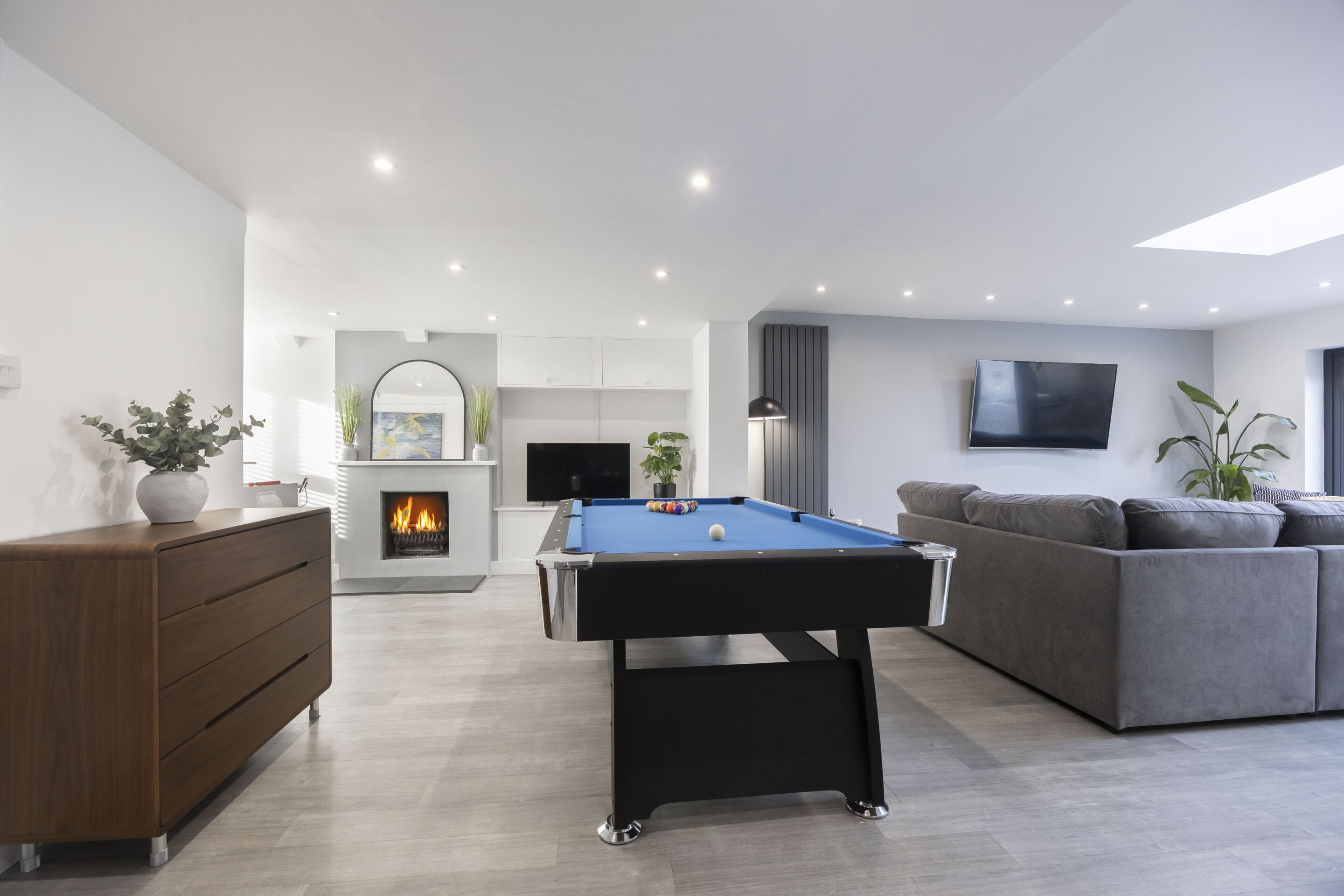 Een moderne woonkamer met een pooltafel, een grijze bank en een open haard.