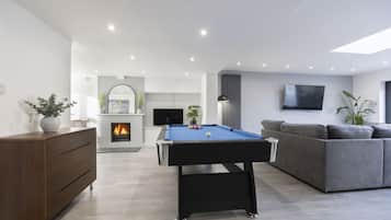 Een moderne woonkamer met een pooltafel, een grijze bank en een open haard.