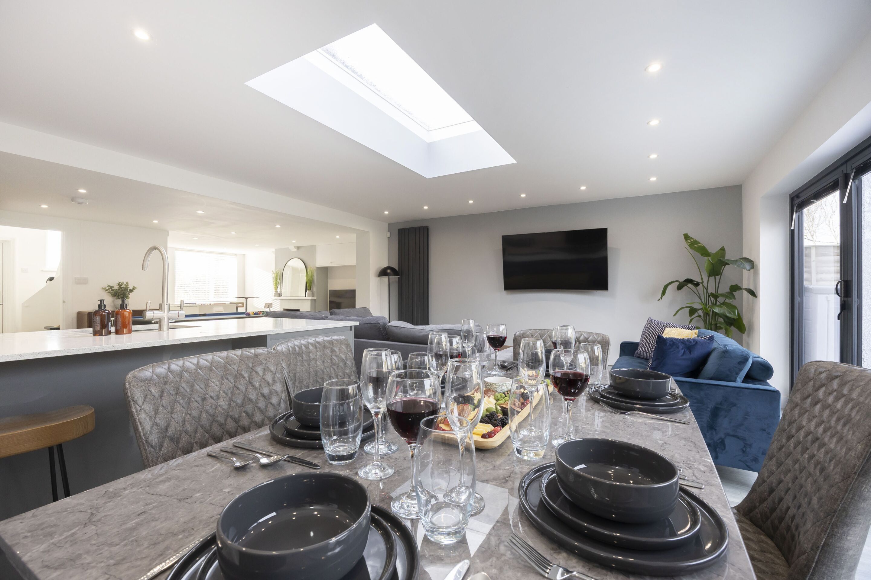 A modern dining area with a high ceiling, skylight, and a flat-screen TV mounted on the wall.