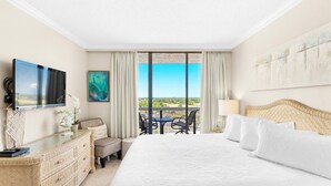 Ein Hotelzimmer mit einem großen Bett, einem Schreibtisch mit Flachbildfernseher, einem Sessel, einem kleinen Tisch und einem Balkon mit Aussicht.