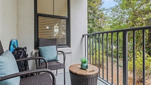 A balcony with wicker furniture, a small round table with a plant, and a view of trees and shrubs. - 2 beach accesses in walking distance! ~1 bd/2ba on 30A~Sleeps 4! (Santa Rosa Beach)