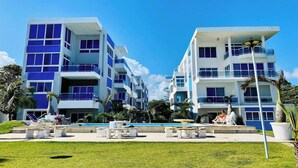 A modern hotel with multiple floors, balconies, and a pool area with lounge chairs and tables. - Beachfront Condo w/ Ocean View, Pool + Steps to Cabarete Beach (Cabarete)