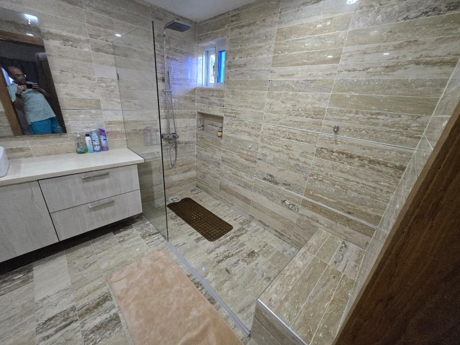 Une salle de bain moderne dotée d’une douche à parois de verre, de carreaux de marbre et d’un meuble-lavabo avec des articles de toilette.