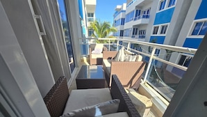 Ein Balkon mit Korbmöbeln, einem Glastisch und Blick auf ein blau-weißes Gebäude mit Balkonen.