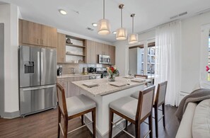 A modern kitchen with stainless steel appliances, a central island with seating, and pendant lighting. - Sea Paradise123 at The Pointe! Large complex pool and hot tub! (Inlet Beach)