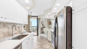 A modern kitchen with white cabinetry, a stainless steel refrigerator, and a dining area with a view. - 3 Bd/3Ba GULF views! Comp Beach chair set-up! (Miramar Beach)