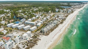 Ett flygbildsbild av en kustort med flera byggnader, en sandstrand och fri utsikt över havet.
