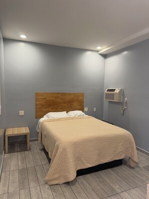 A bedroom with a bed, a nightstand, a wooden headboard, a wall-mounted air conditioner, and a ceiling light. - Casa Motel (Los Angeles)