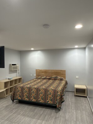 A bedroom with a bed, a wooden headboard, a wall-mounted heater, and a small bedside table. - Casa Motel (Los Angeles)