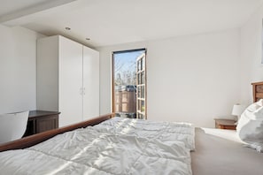 A bedroom with a bed, a wardrobe, a nightstand, and a window. - Lovely holiday home near forest and beach (Aabenraa)
