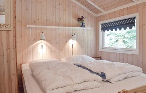 A wooden-paneled room with a bed, two wall-mounted lamps, a window with a view, and a shelf with a vase.