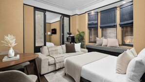 Een hotelkamer met een bed, een slaapbank, een eettafel, een televisie en een raam met gordijnen.