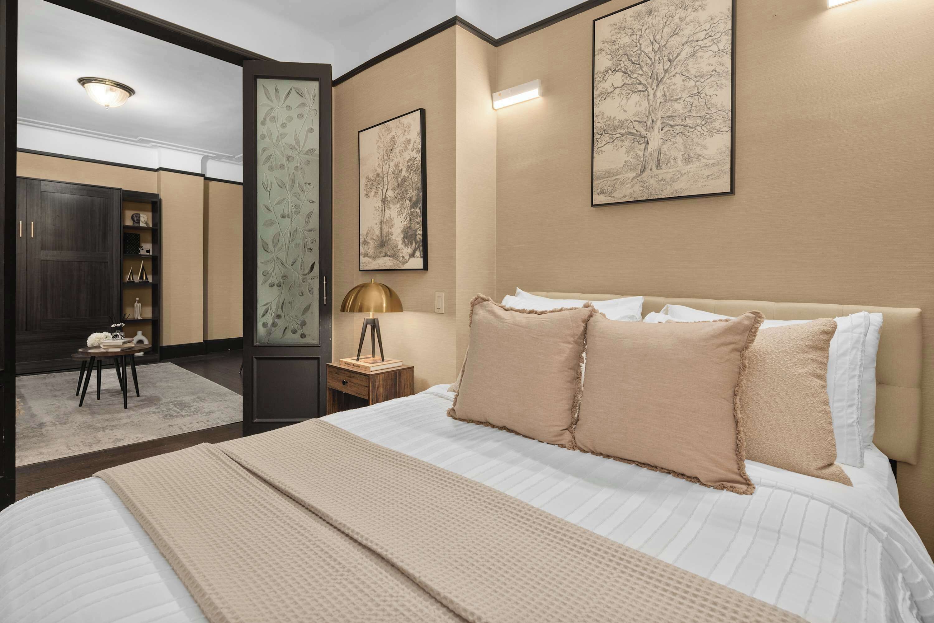 A bedroom with a large bed, a bedside table with a lamp, and two framed artworks on the wall.