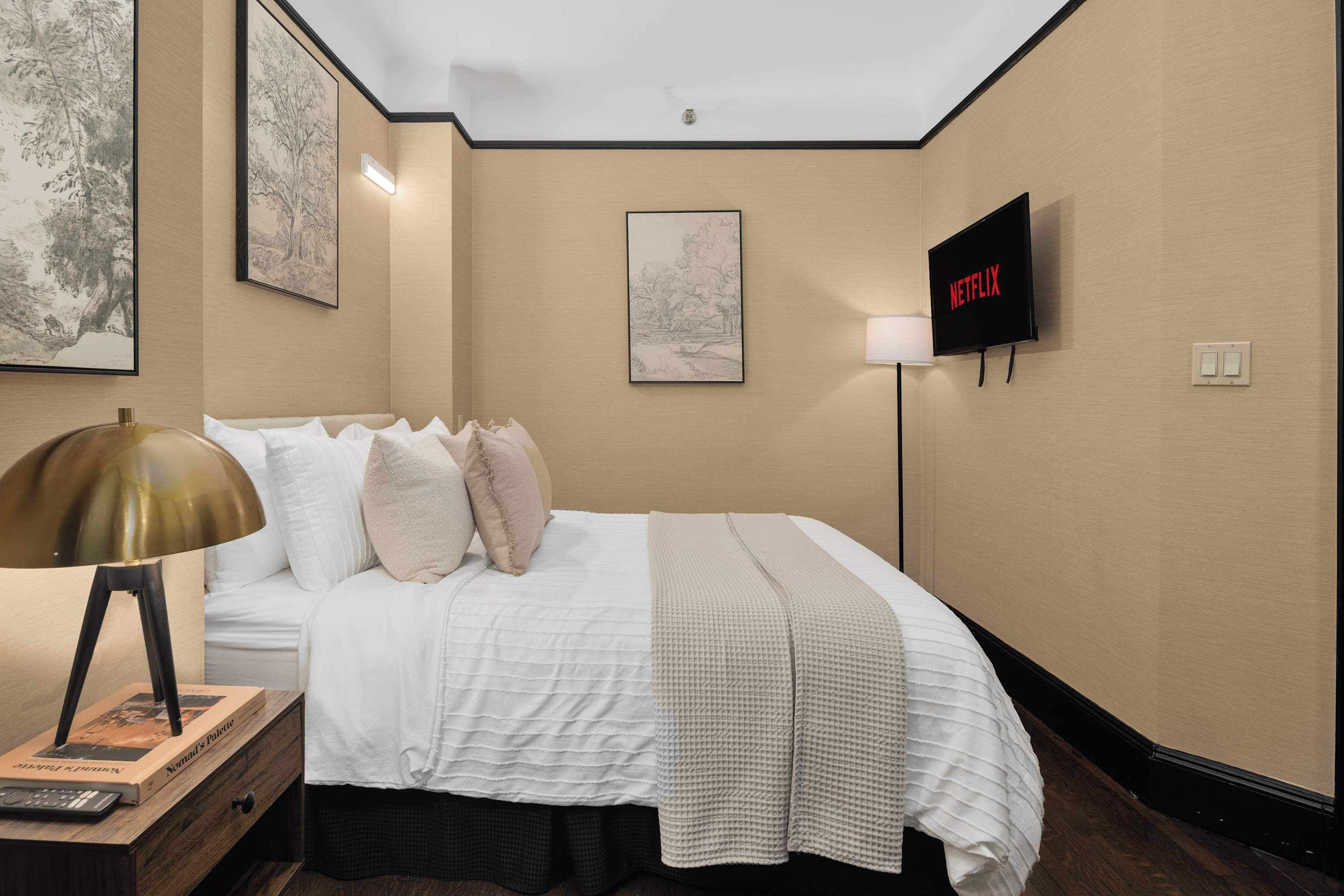 Una camera d'albergo con un letto rifatto, una lampada da comodino, una TV a schermo piatto e quadri appesi alle pareti.