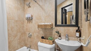 Een badkamer met een bad, toilet, wastafel en een spiegel. Er staan toiletartikelen aan de muur en een mandje op het toilet.