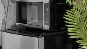 Een keuken met een koffiezetapparaat, magnetron en een kleine koelkast.
