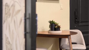 Une pièce avec une table en bois, deux chaises, un téléviseur fixé au mur qui affiche le logo « NETFLIX », et une porte dotée d’un cadre sombre.