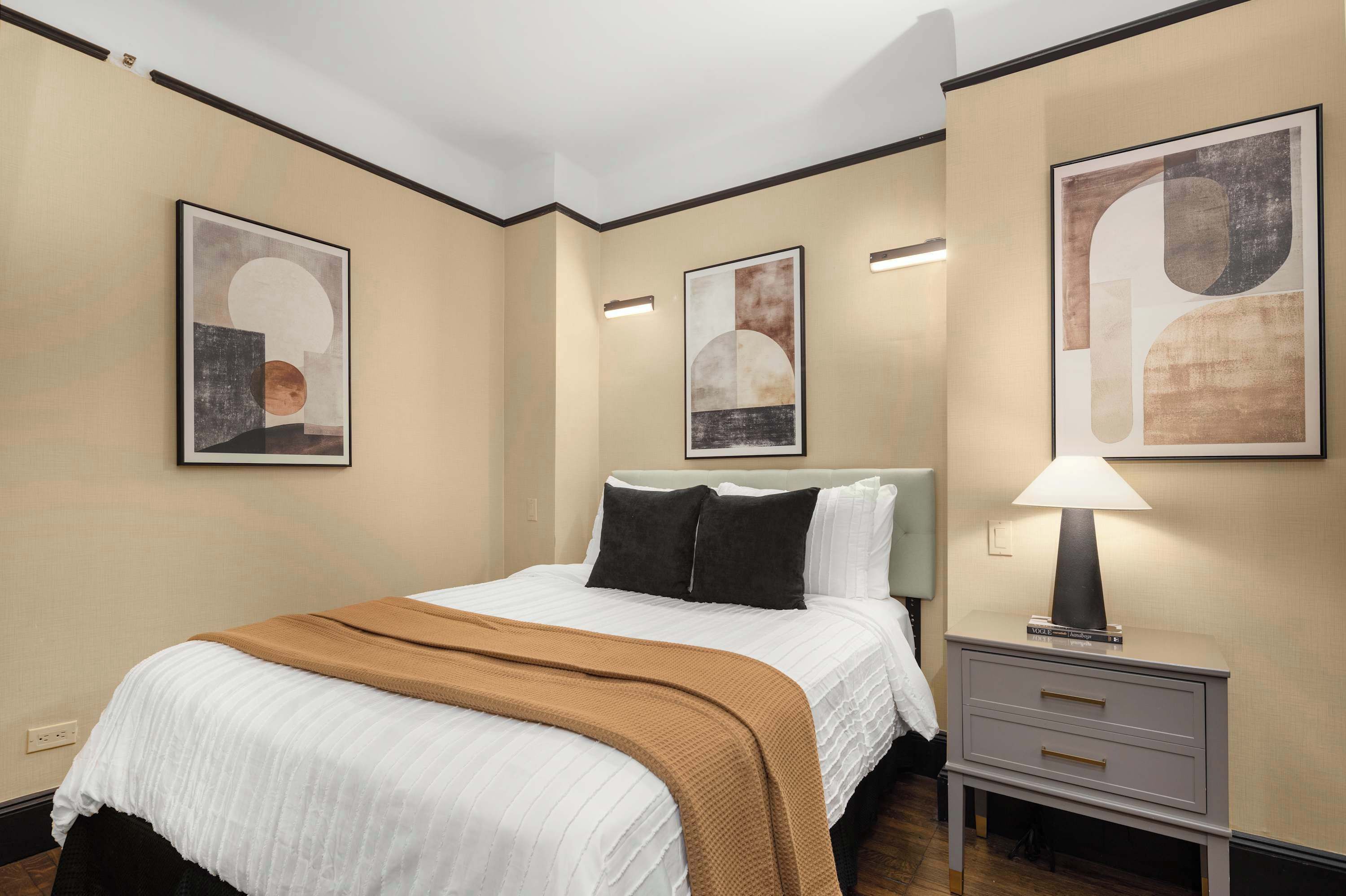 Une chambre d’hôtel avec un lit, une table de chevet avec une lampe et des œuvres d’art abstraites accrochées au mur.