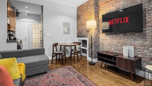 A modern living room with a brick wall, a flat-screen TV, a fireplace, and a dining area.