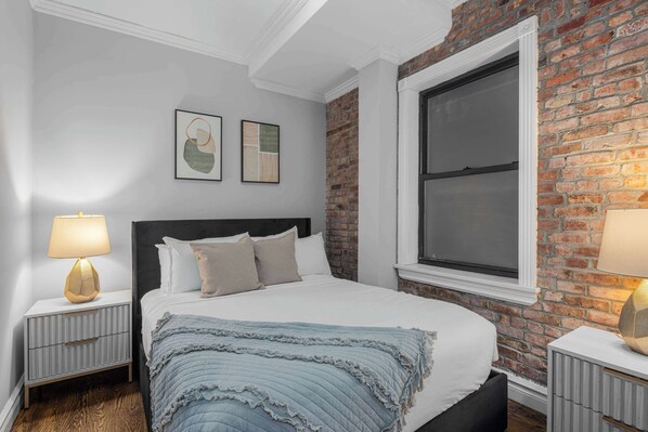 Un dormitorio con una cama grande, una pared de ladrillo, una ventana y dos mesitas de noche con lámparas.