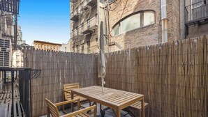 A wooden table and chairs set on a balcony with a bamboo fence, overlooking a cityscape.