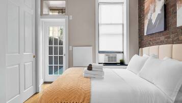 A bedroom with a large bed, a window with blinds, a radiator, and a door.