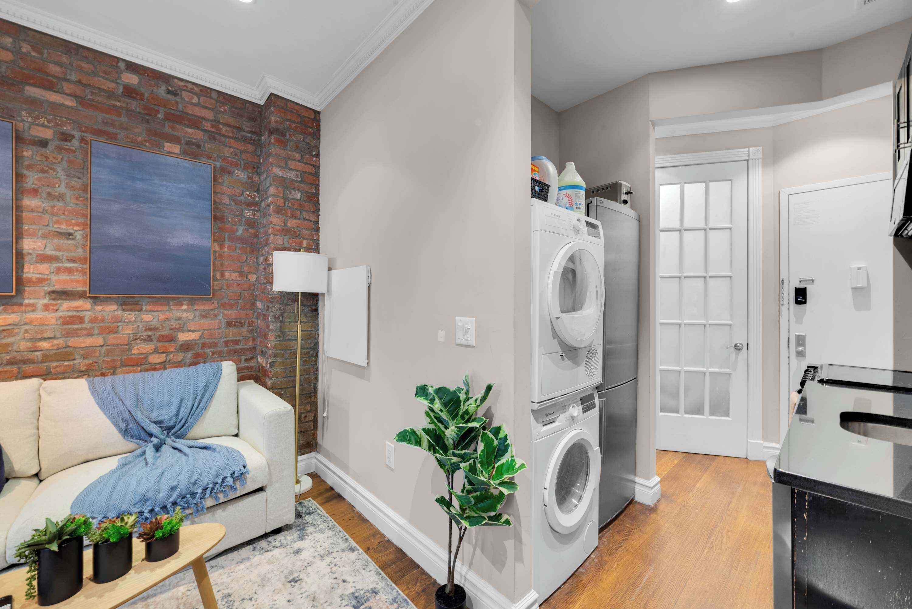 A modern laundry room with a washing machine and dryer, a white door, and a brick wall.