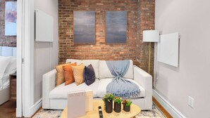Ein modernes Wohnzimmer mit einem weißen Sofa, einer Ziegelwand, zwei gerahmten Kunstwerken, einer Lampe und einem kleinen Tisch mit Pflanzen.