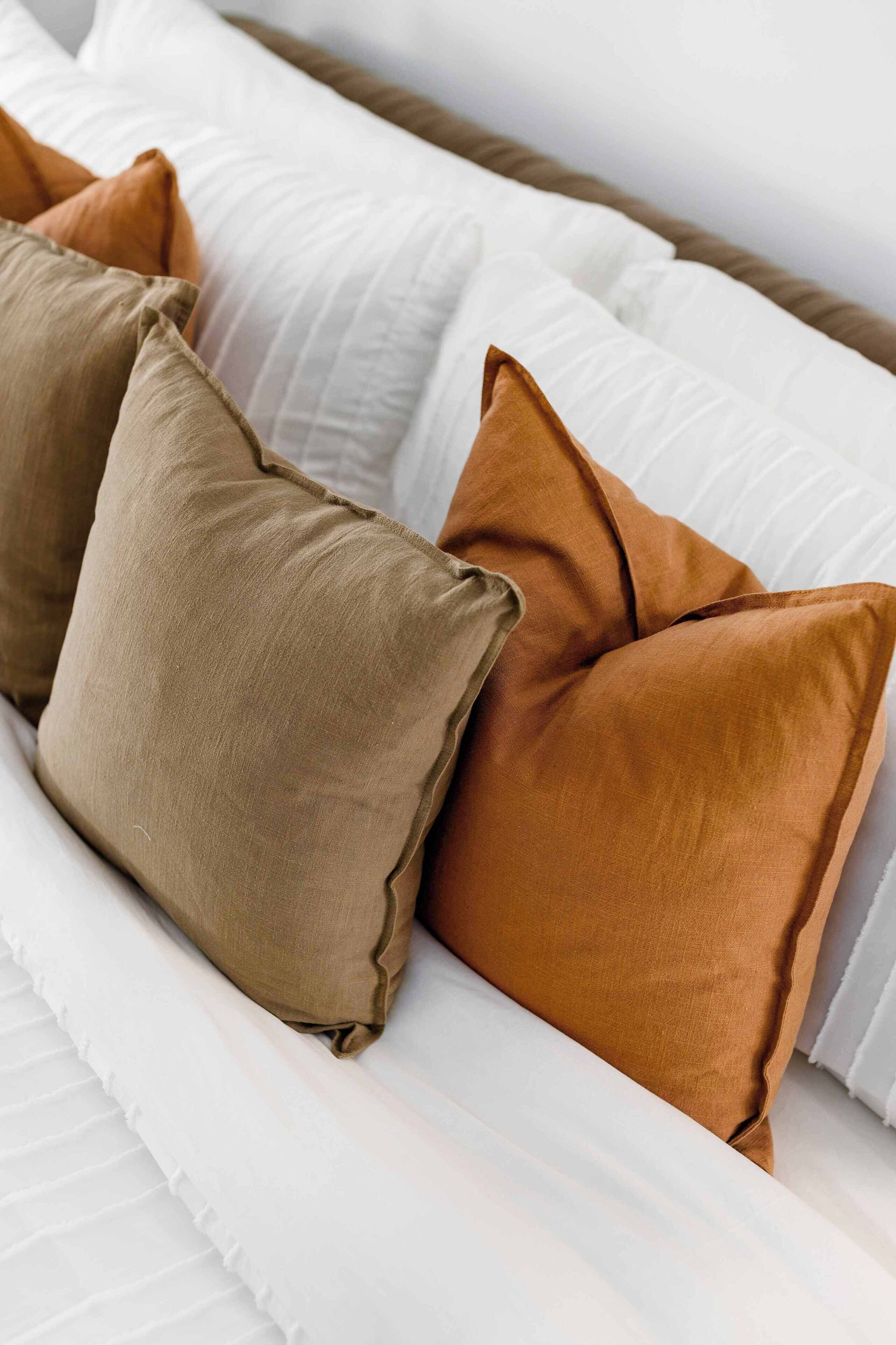 A bed with white bedding and two pillows, one brown and one tan.
