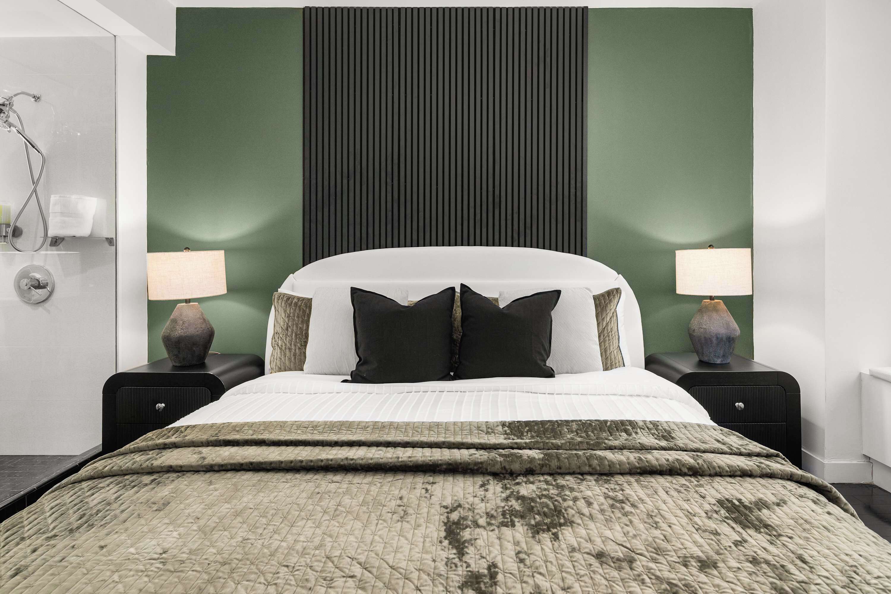 A neatly made bed with a green and white duvet, two bedside lamps, and a green accent wall.
