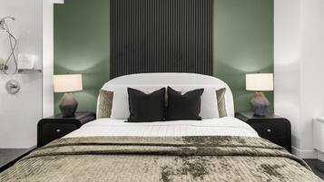 A neatly made bed with a green and white duvet, two bedside lamps, and a green accent wall.