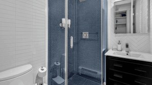 Ein Badezimmer mit Duschkabine, Toilette in Weiß und Waschbecken mit Spiegel darüber.
