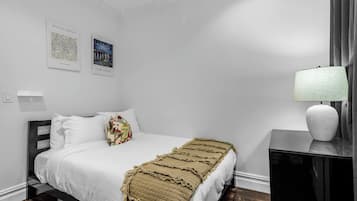 A bedroom with a bed, a bedside table with a lamp, and two framed artworks on the wall.