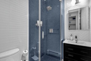 Un baño con cabina de ducha de vidrio, inodoro blanco y lavamanos con espejo.