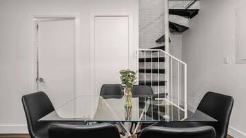 Un espace repas moderne avec une table en verre et des chaises noires, une porte blanche et un escalier avec un mur blanc et des rampes noires.