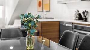 Uma sala de jantar moderna com mesa de vidro, cadeiras e um vaso com folhagem verde.