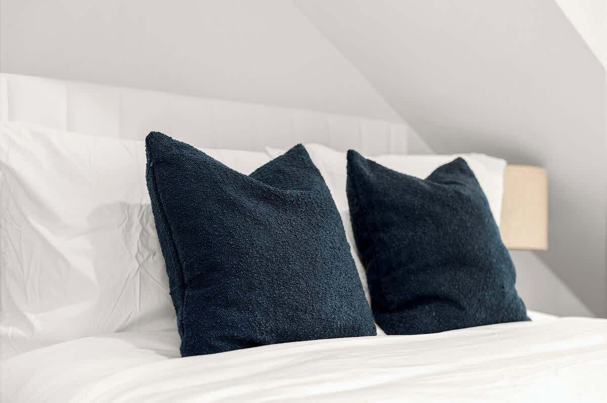 A neatly made bed with white linens and two dark blue pillows.