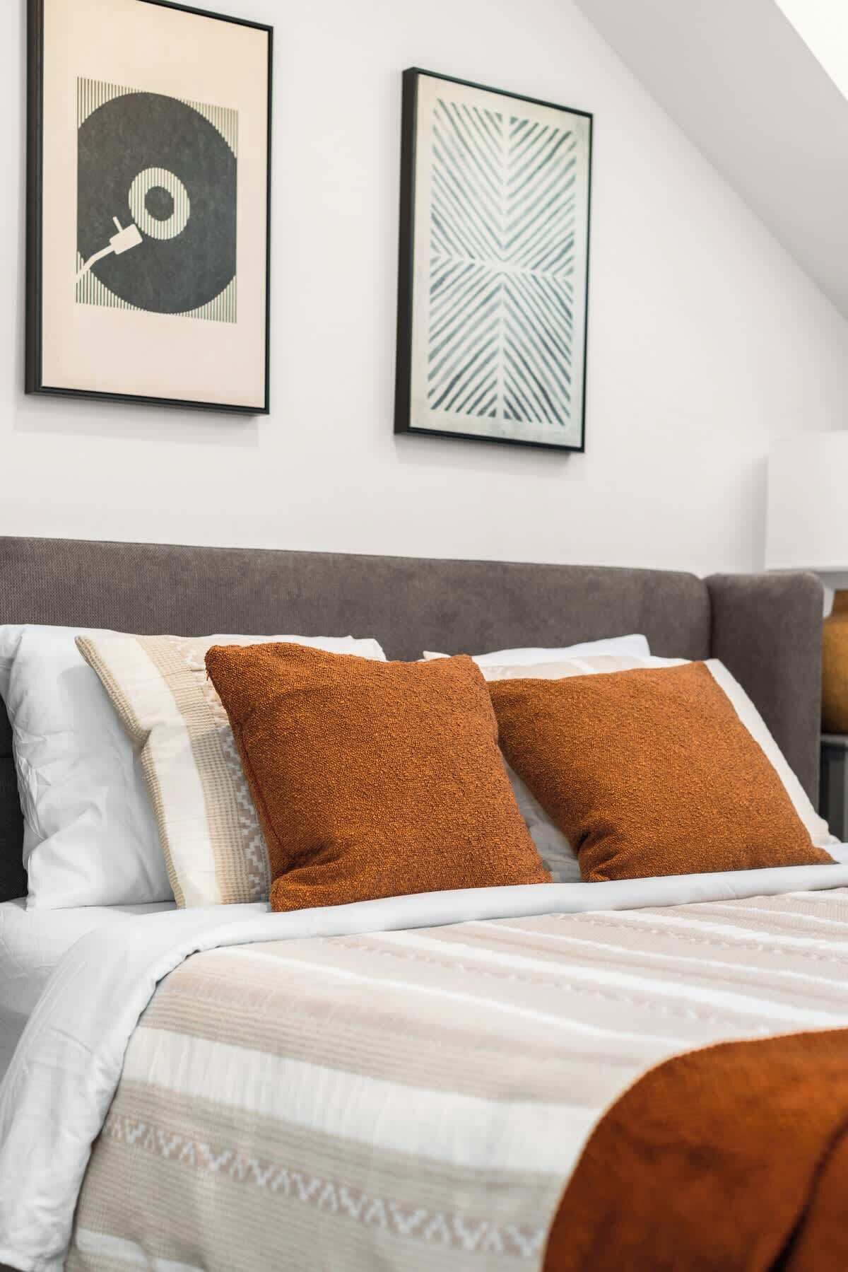 A bedroom with a bed, pillows, and two framed artworks on the wall.