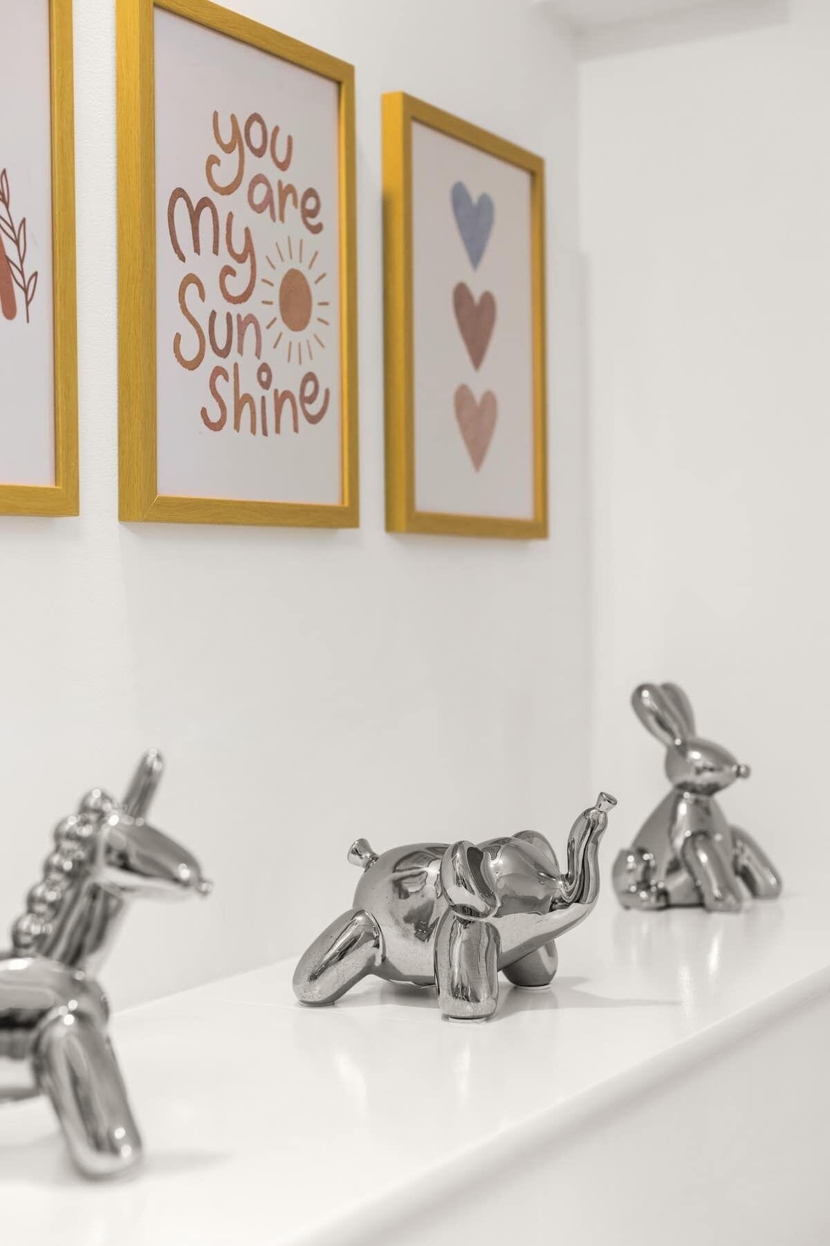 Decoración mural en marco con frases motivacionales y símbolos de corazón, junto con figuras de animales plateadas sobre un estante blanco.