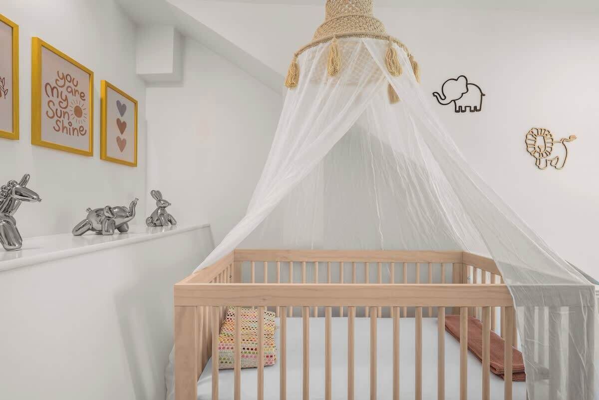 Una cuna con dosel blanco, un estante con figuritas decorativas de animales y decoración de pared con mensajes positivos.