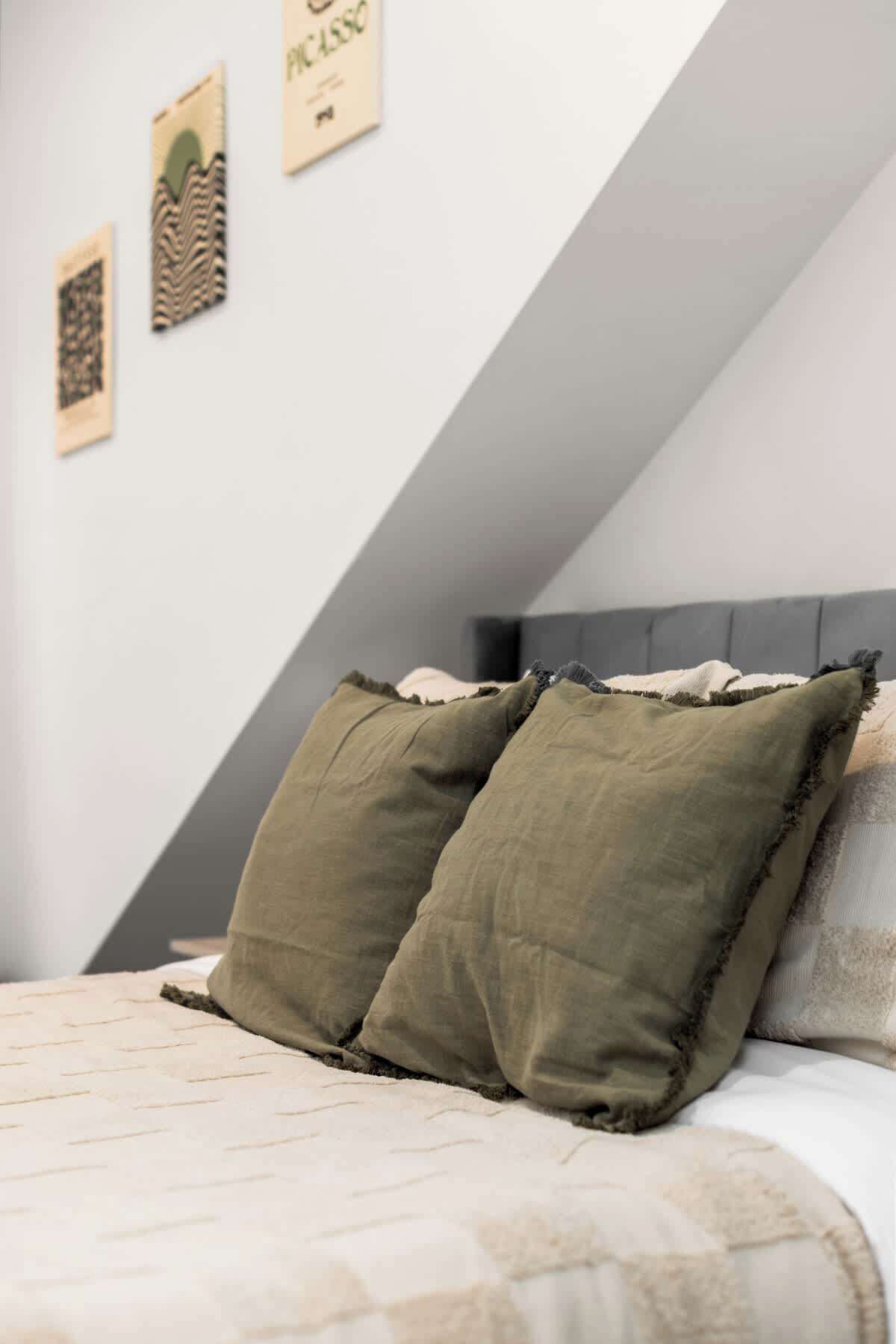 Een slaapkamer met een schuine kap, een bed met een gewatteerde spreidek en drie ingelijste kunstwerken aan de muur.