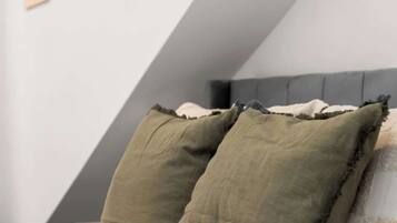 Een slaapkamer met een schuine kap, een bed met een gewatteerde spreidek en drie ingelijste kunstwerken aan de muur.
