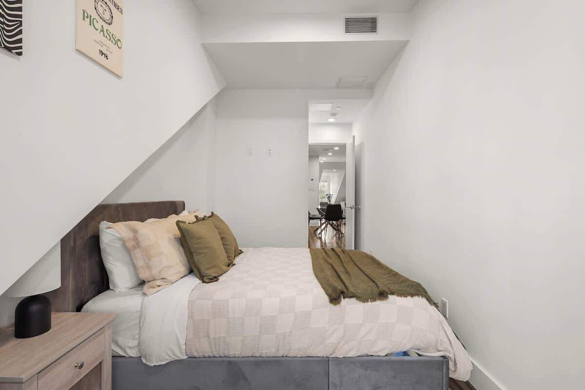 Een slaapkamer met een bed, nachtkastje en een kunstwerk aan de muur.
